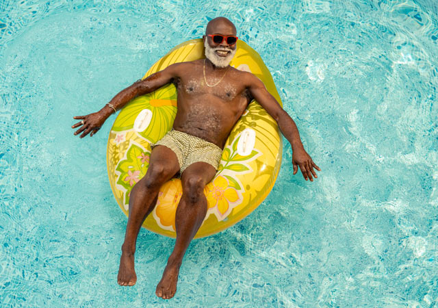 A person lounging on a bright floral inflatable raft in a clear blue swimming pool.