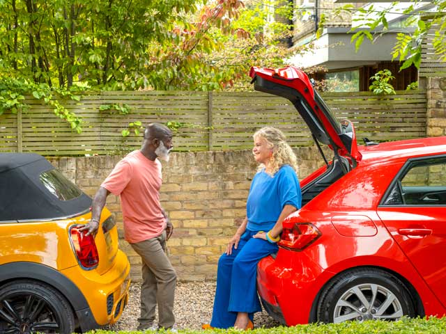 Two people chatting behind their cars