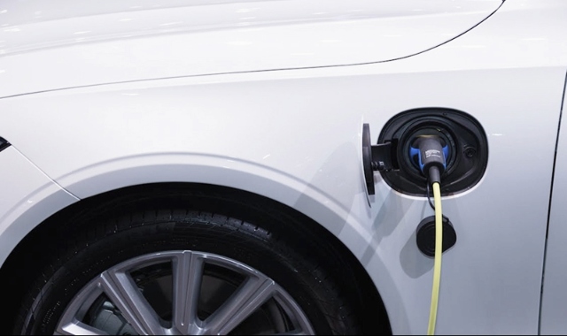 A close-up of an electric car with a charging cable plugged into its side port.
