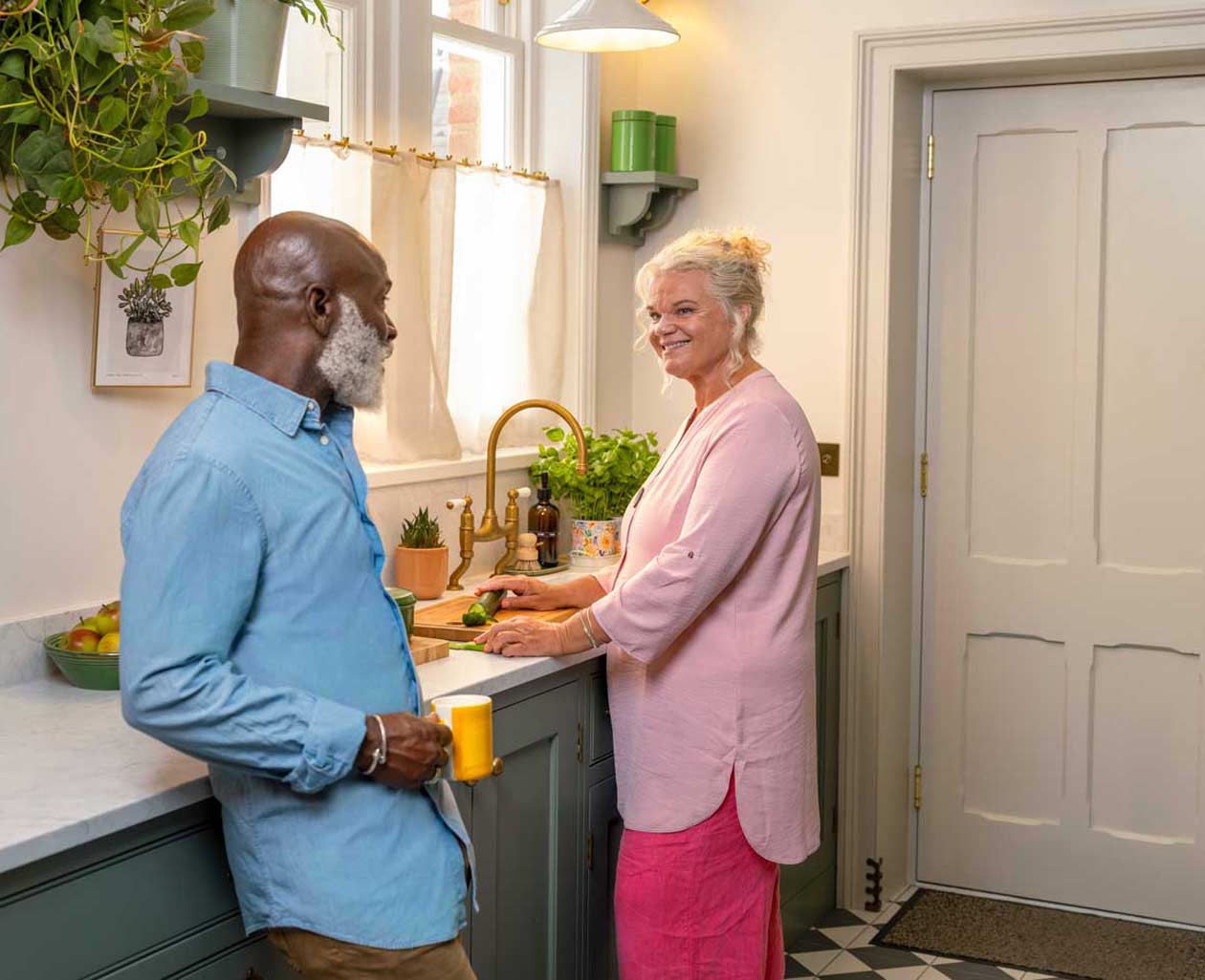 Two people standing together in a kitchen, smiling and engaged in conversation.