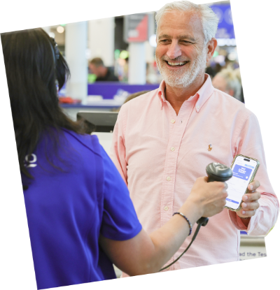 A smiling customer interacts with a friendly Tesco colleague scanning their mobile app at checkout.