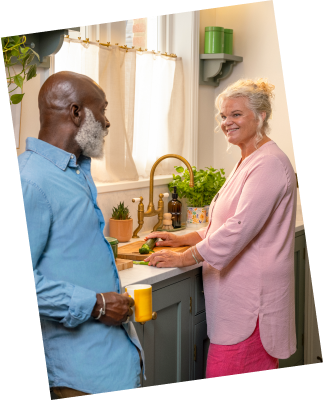 Two people standing together in a kitchen, smiling and engaged in conversation.