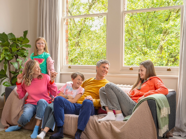 A family of five, including parents and children, play together on a couch.