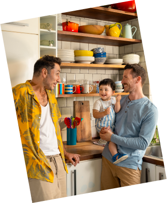 Two adults and a child smiling together in a cheerful kitchen, with plates and utensils in the background.