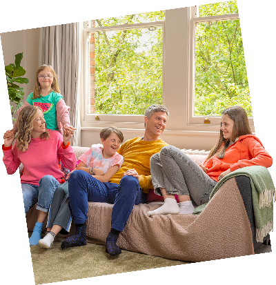 A family and their dog enjoy time together seated on a couch in front of a large window.